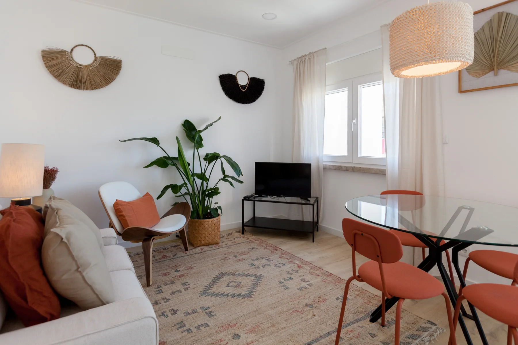 A bright living and dining area with seating, a television, and a glass table.