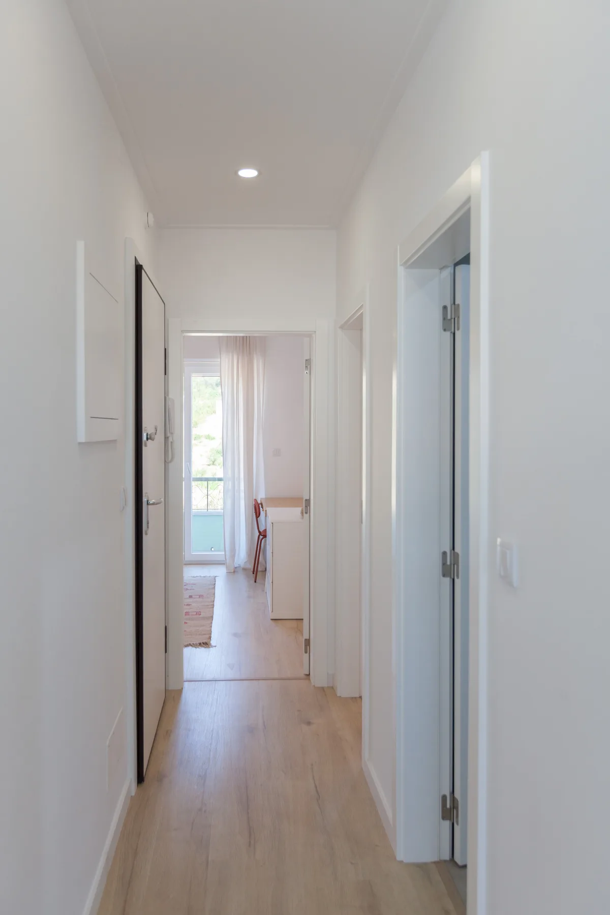 A bright hallway leads to a room with a window and a small table.