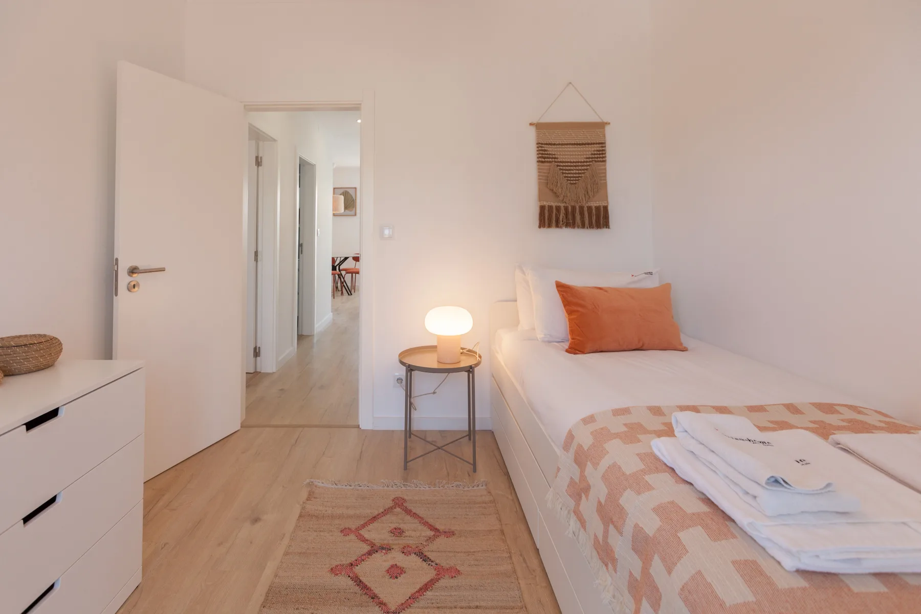 A bedroom with a single bed, bedside table, and lit lamp.