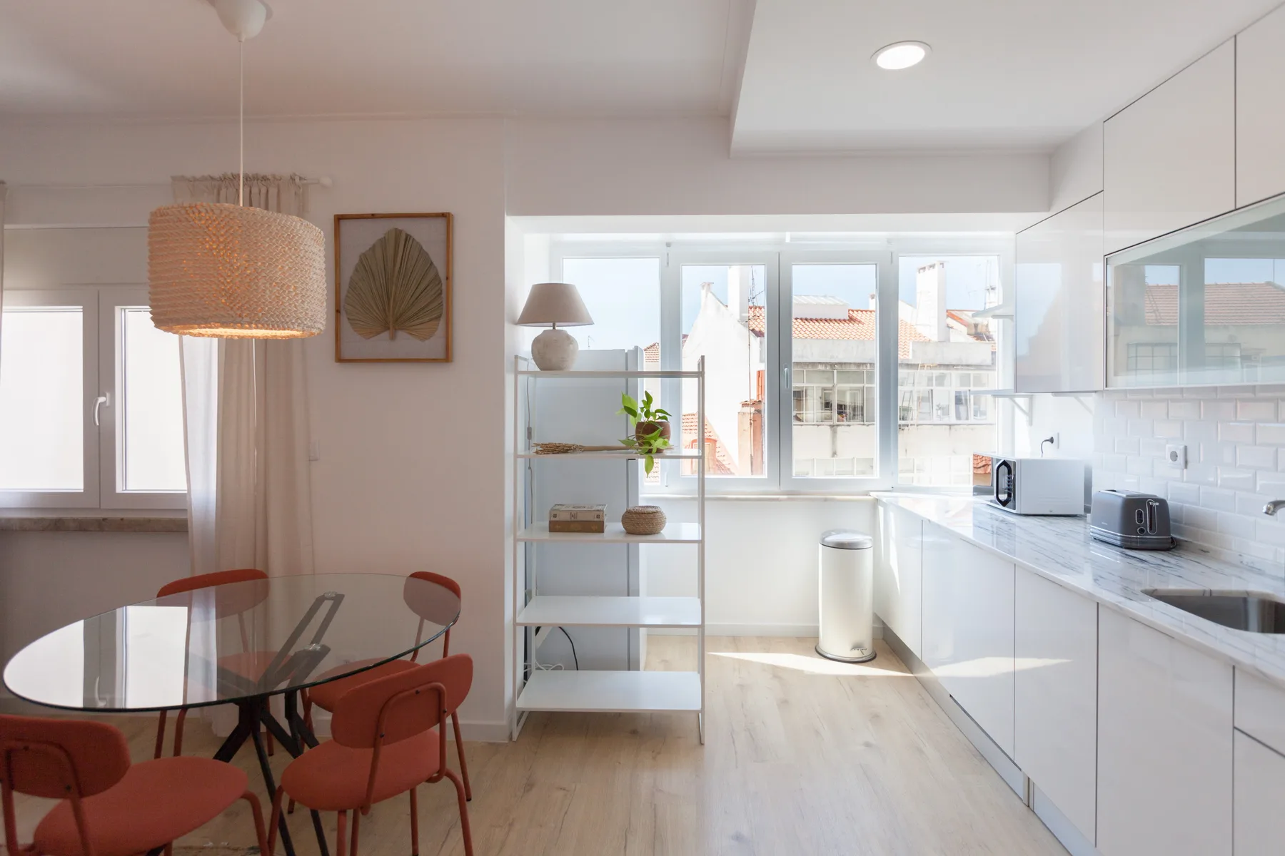 A bright open-plan kitchen and dining area with white cabinetry and a glass dining table.
