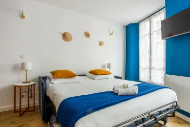 Un dormitorio con una cama grande, ropa de cama azul y ventanas altas.