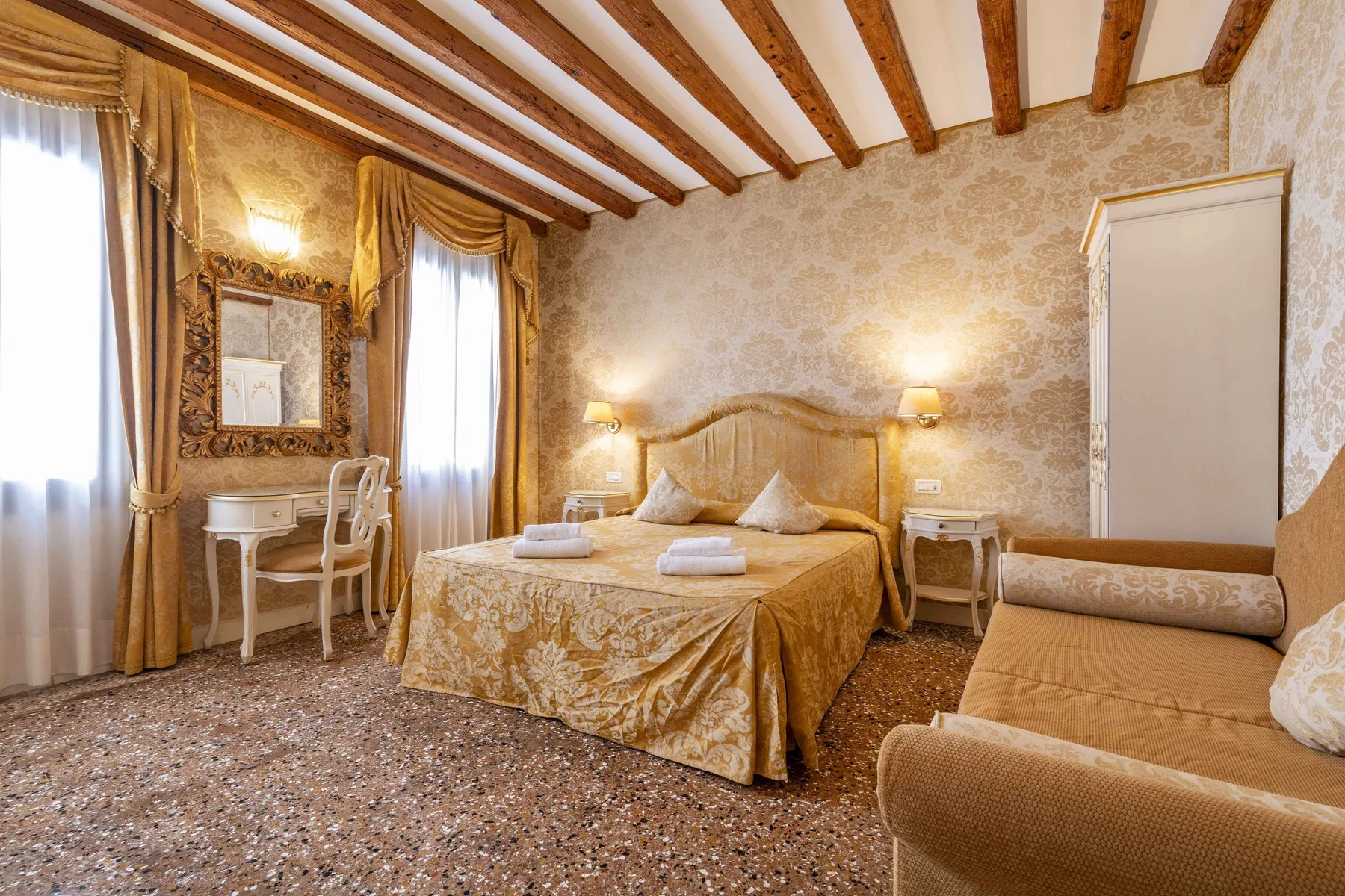 A bedroom with a large bed, a writing desk, and upholstered seating.