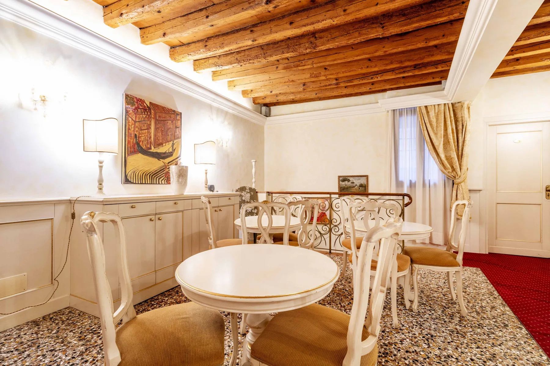 A dining area with a round table and ornate railing beneath exposed wooden beams.