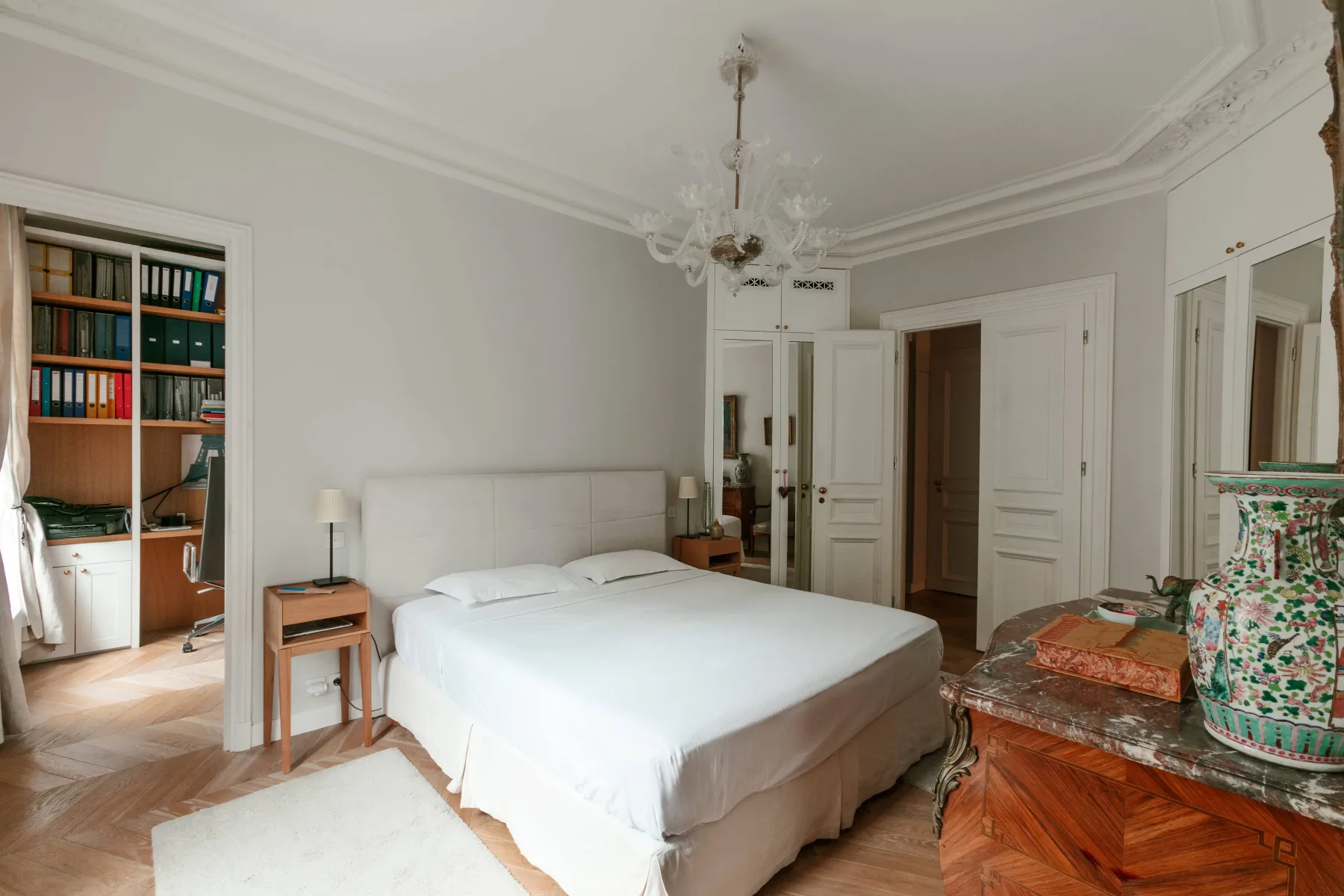A bedroom with a neatly made bed, built-in cabinets, and a chandelier.
