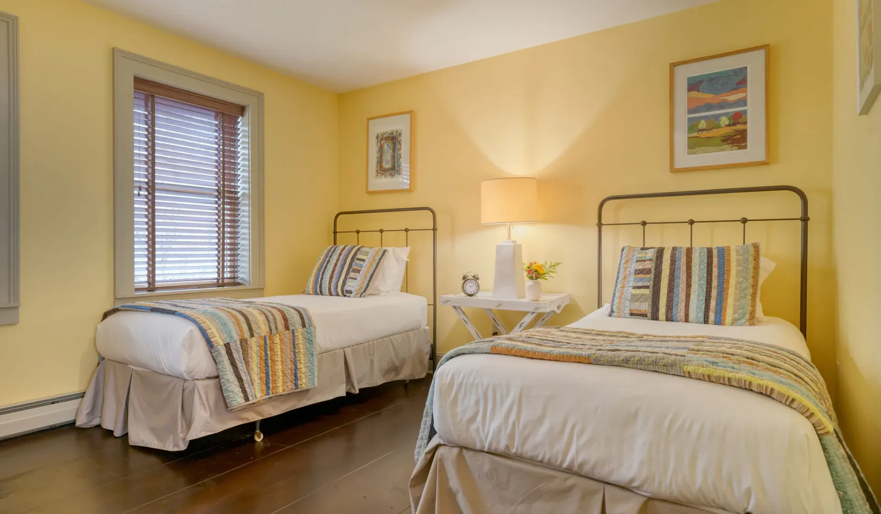 Un dormitorio amarillo con dos camas, ropa de cama estampada y cuadros en la pared.