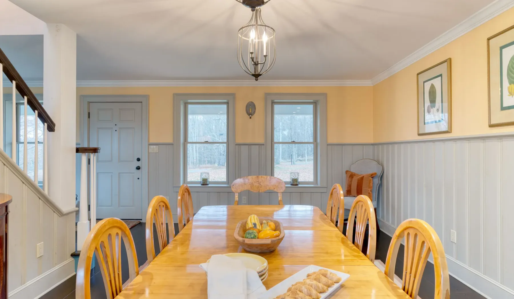 Un comedor con una mesa larga de madera, sillas y ventanas.