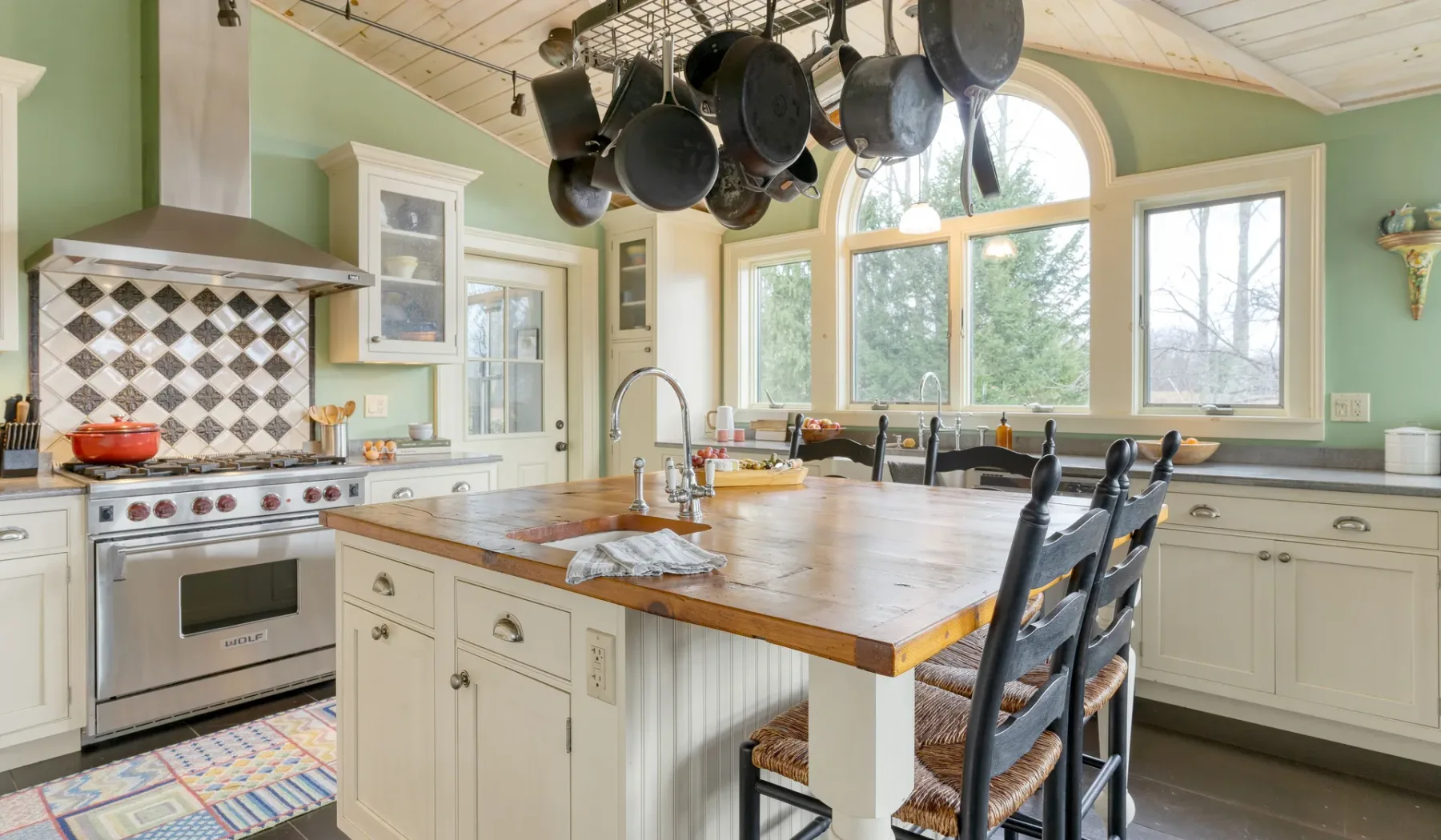 Una cocina luminosa con una gran isla de madera y utensilios de cocina colgantes.