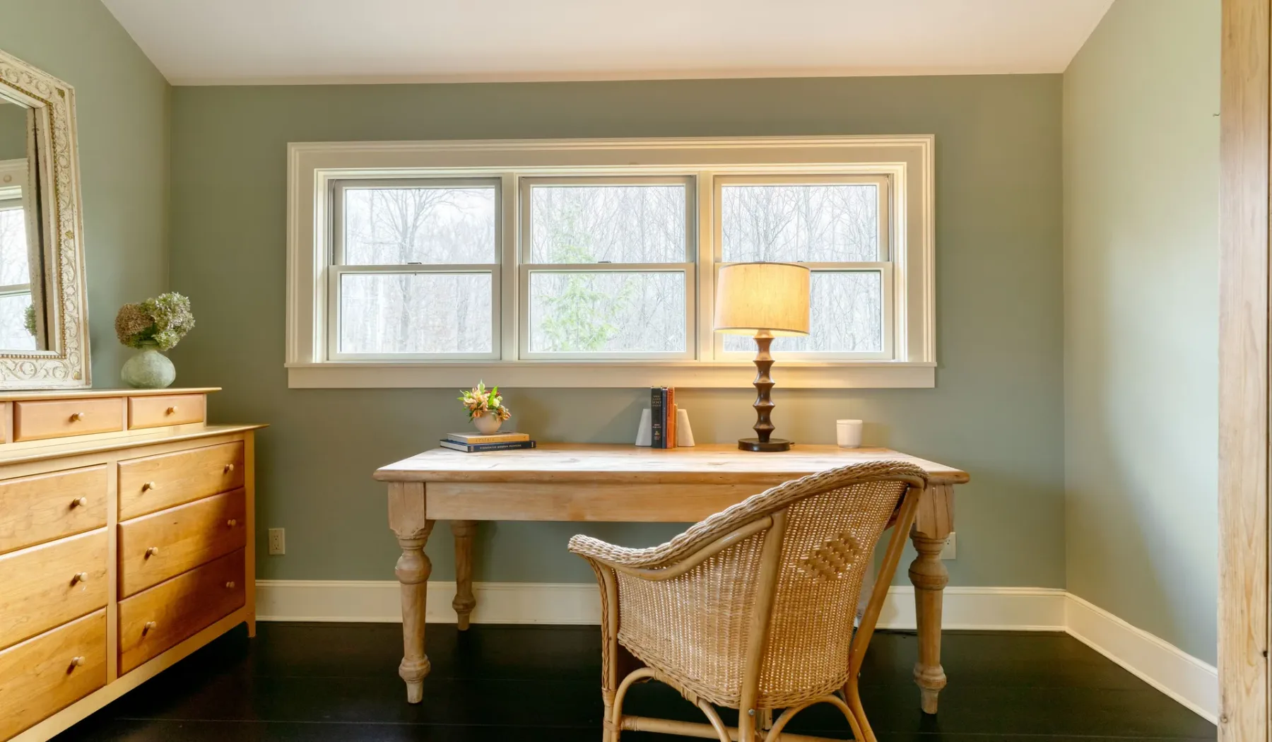 Un despacho con escritorio de madera, asiento de mimbre y una ventana amplia.