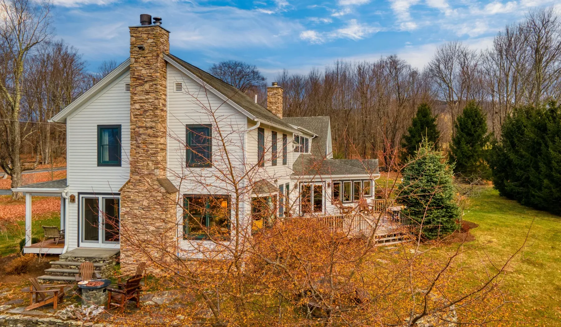 Una casa grande con una chimenea de piedra está junto a un patio verde y árboles.