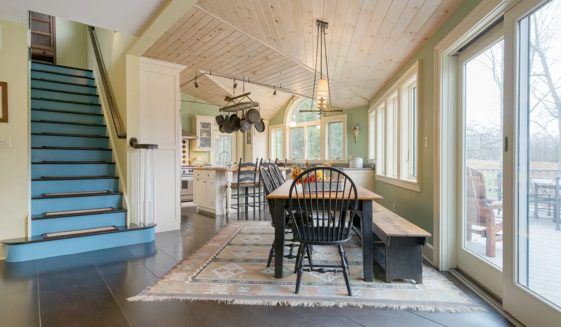 Un comedor con una mesa larga está junto a una cocina luminosa y ventanas grandes.
