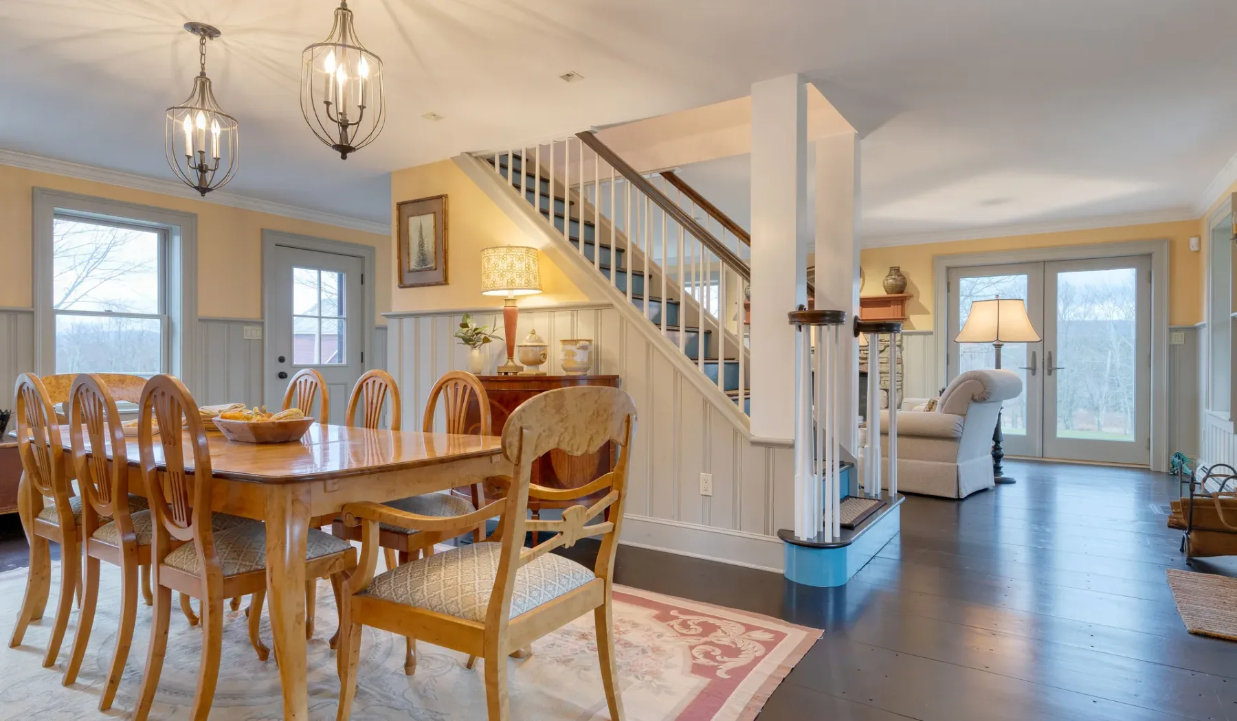 Comedor con una mesa de madera junto a una escalera y una sala contigua.