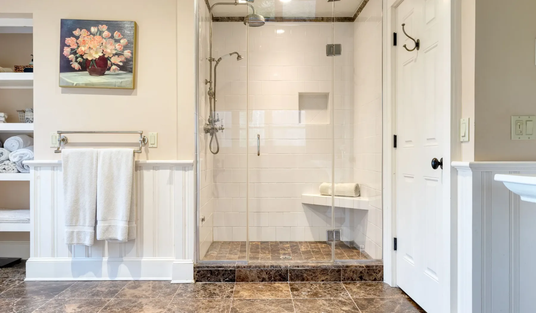 Un baño luminoso cuenta con una ducha con paneles de vidrio y azulejos blancos.