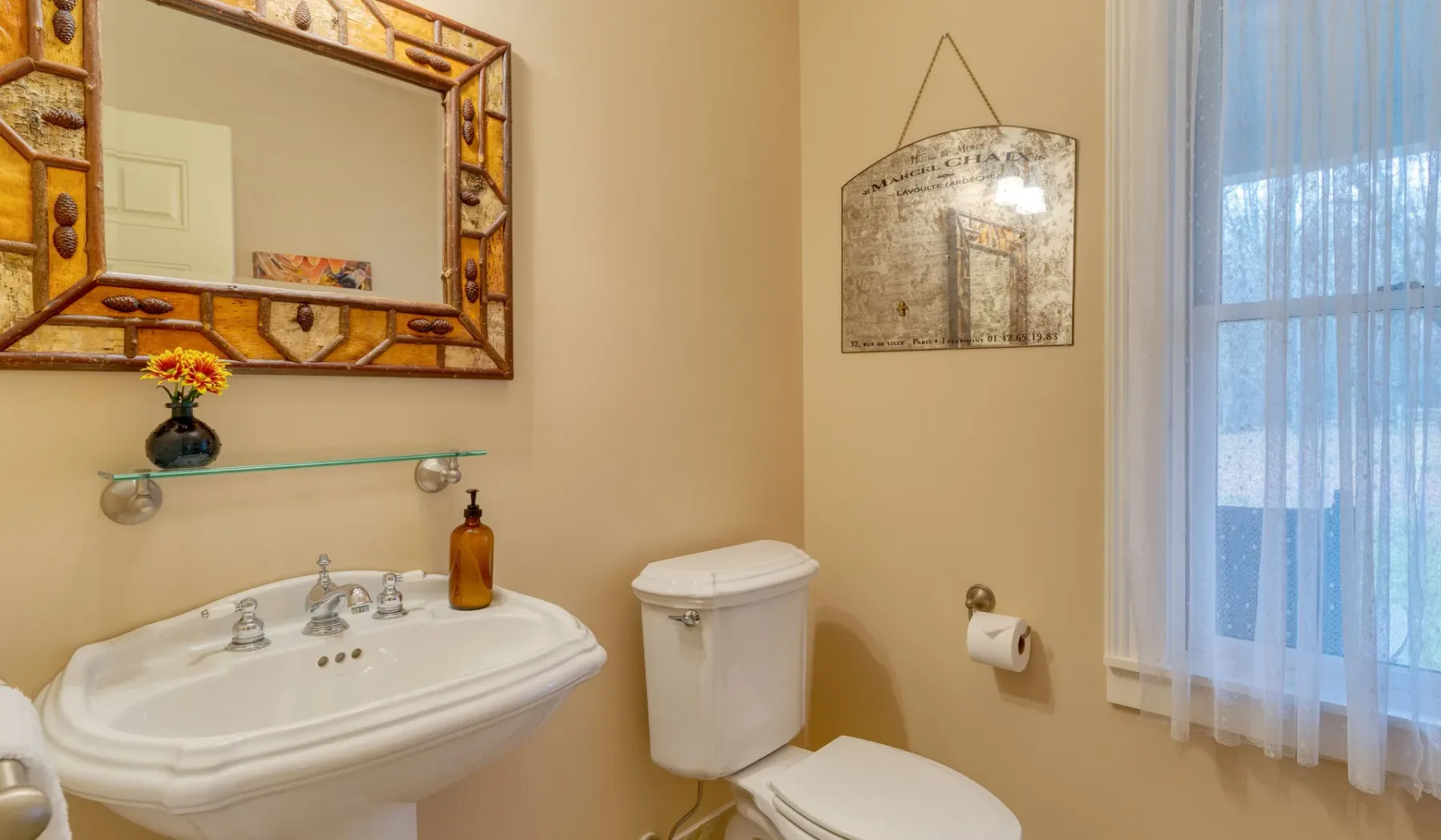 Un baño con lavabo, inodoro y una ventana con cortinas transparentes.