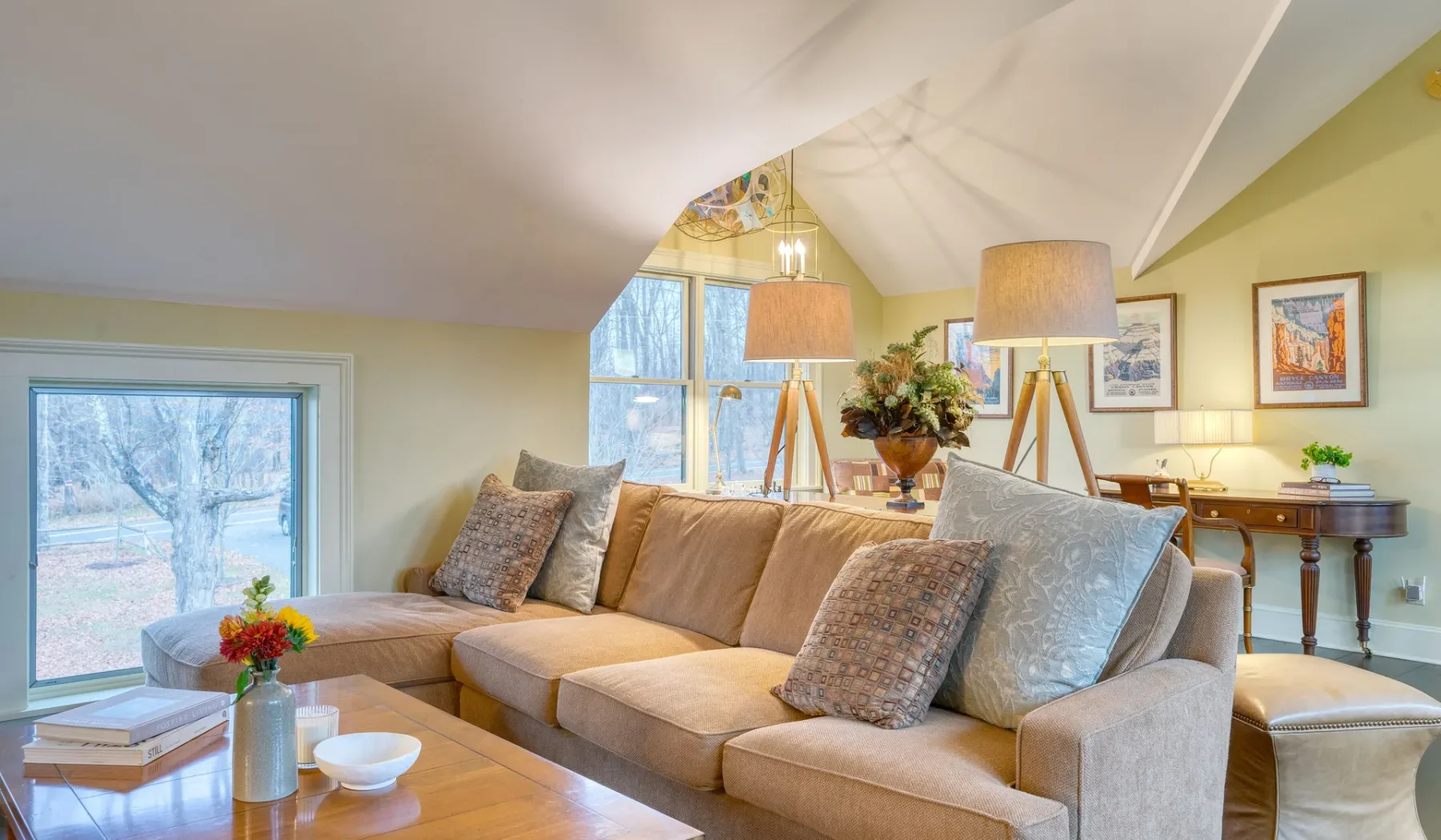 Una sala luminosa cuenta con un sofá seccional, ventanas grandes y una mesa de centro.