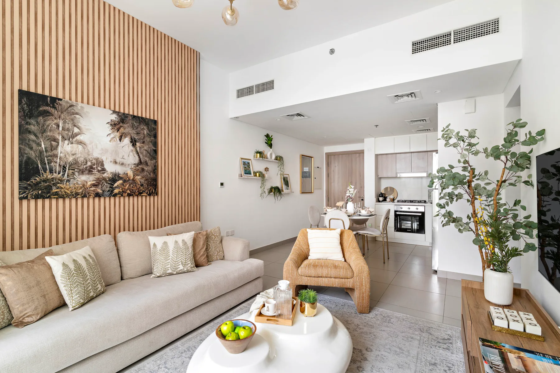 A living room opens into a kitchen, with light-colored seating and a wood-slat accent wall.