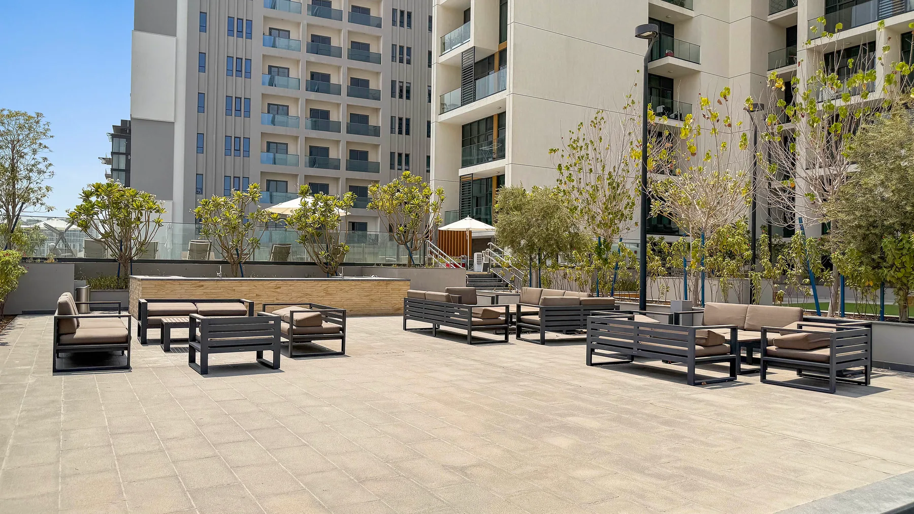 An outdoor terrace with several seating areas sits beside a modern apartment building.
