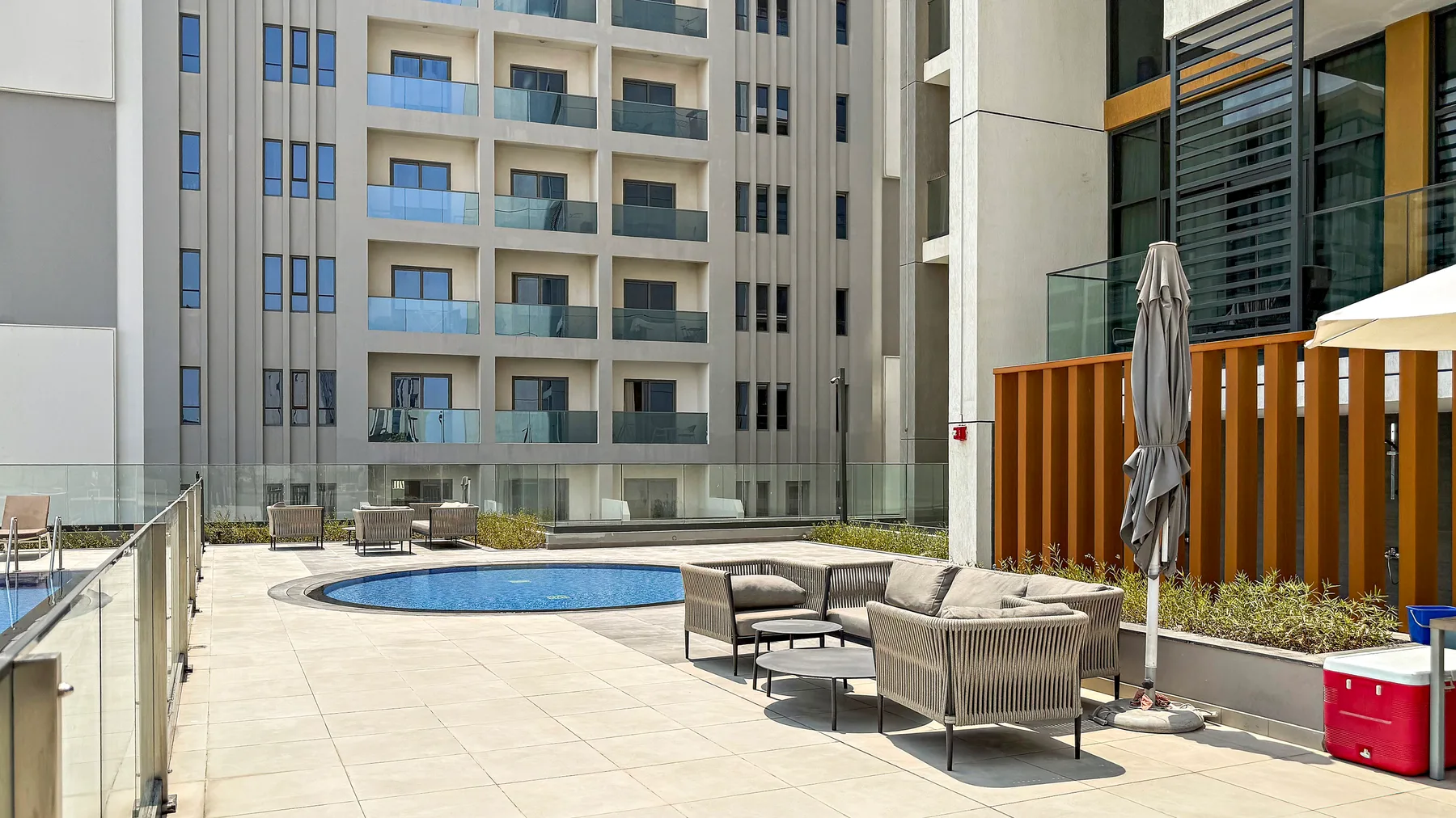 A sunny outdoor patio has a small swimming pool and seating beside the building.
