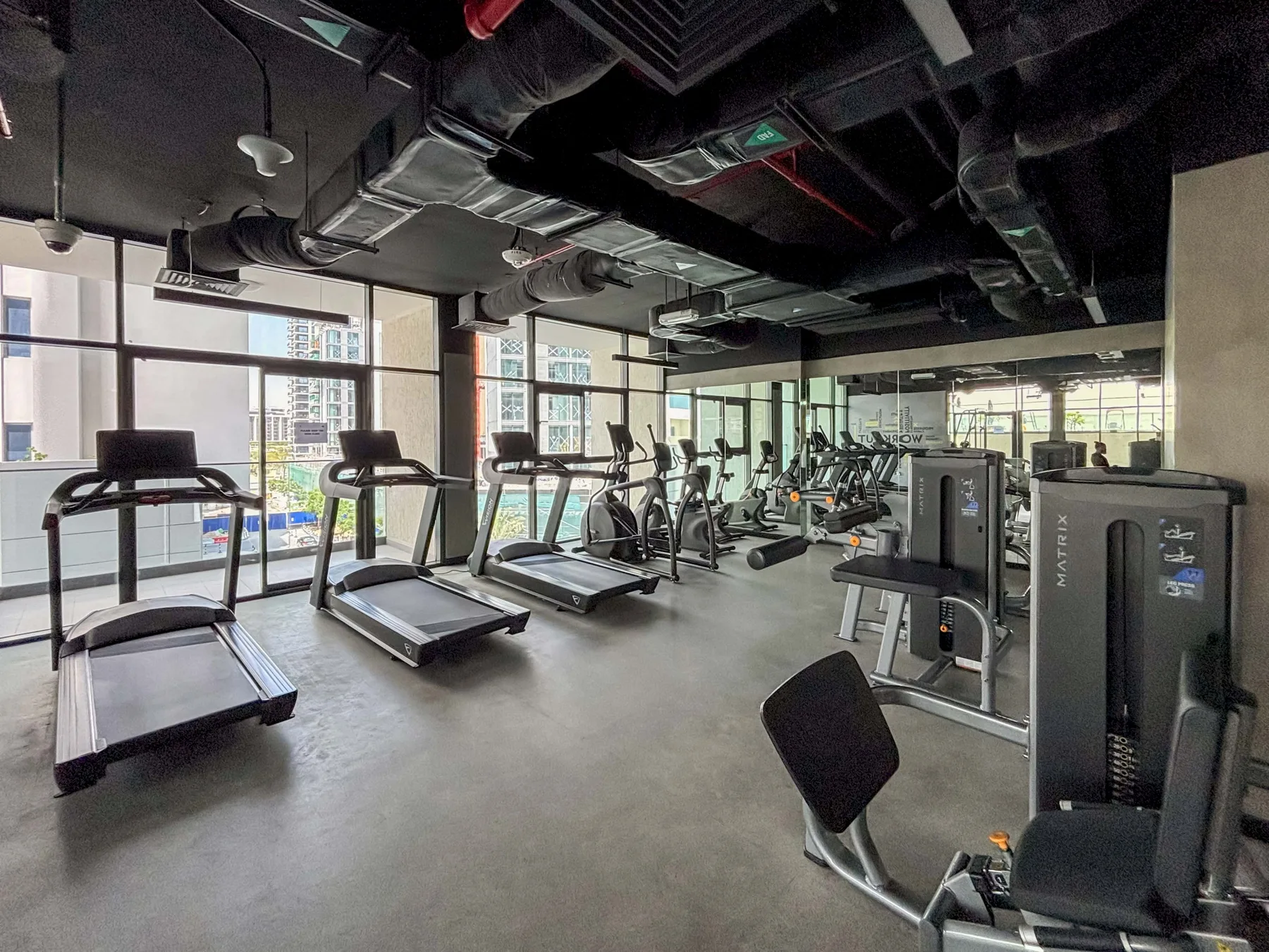 A fitness room with treadmills and exercise equipment beside large windows.