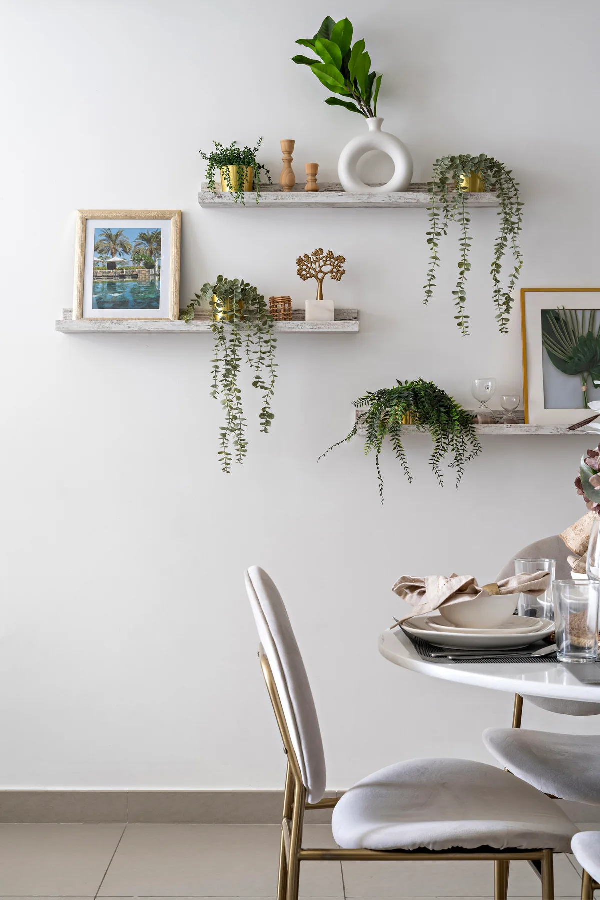 A bright dining area with floating shelves displaying plants, framed art, and decorative objects.
