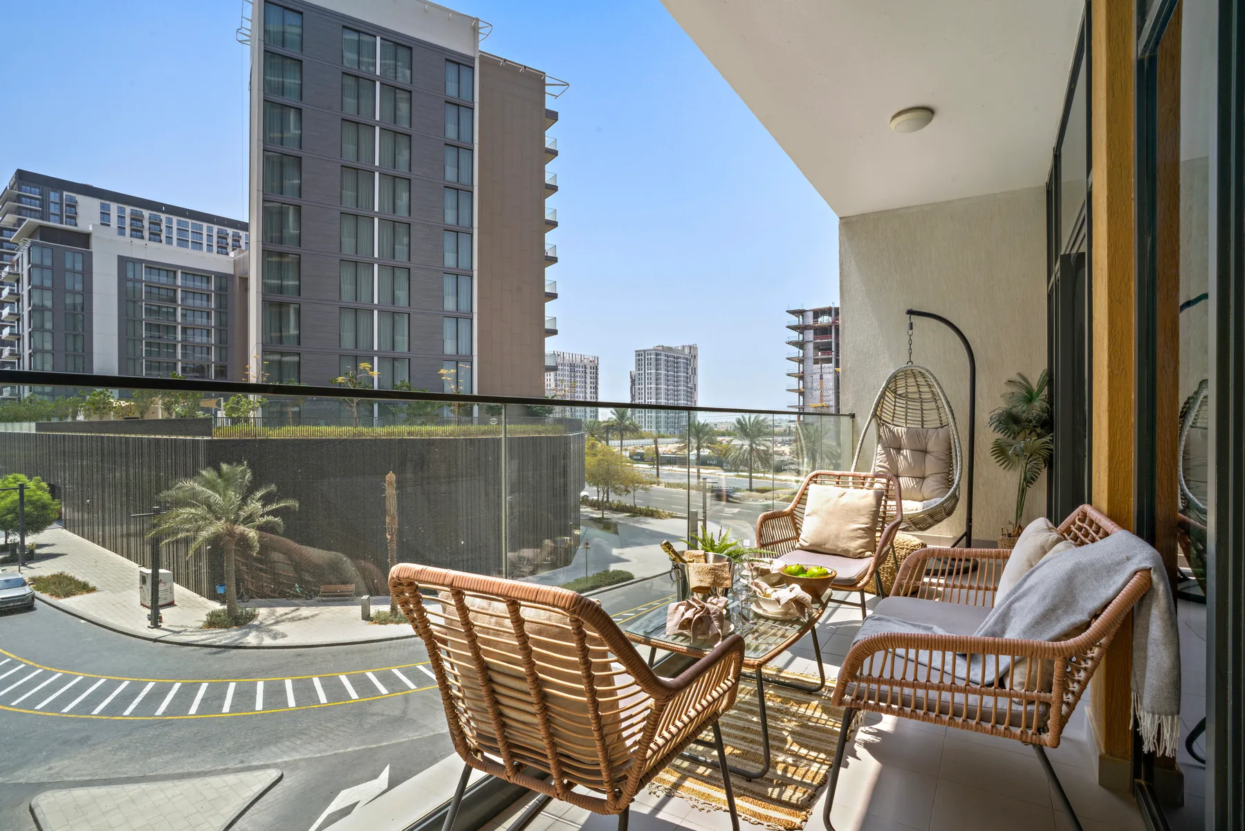 A balcony seating area with wicker furniture overlooks nearby buildings and a street.