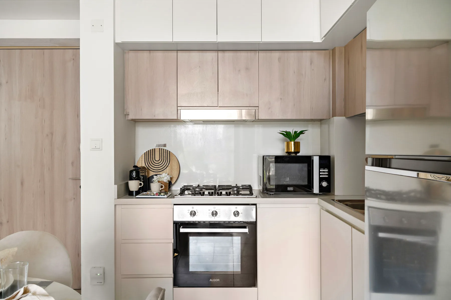 A modern kitchen with pale wood cabinets, a stovetop, and an oven.