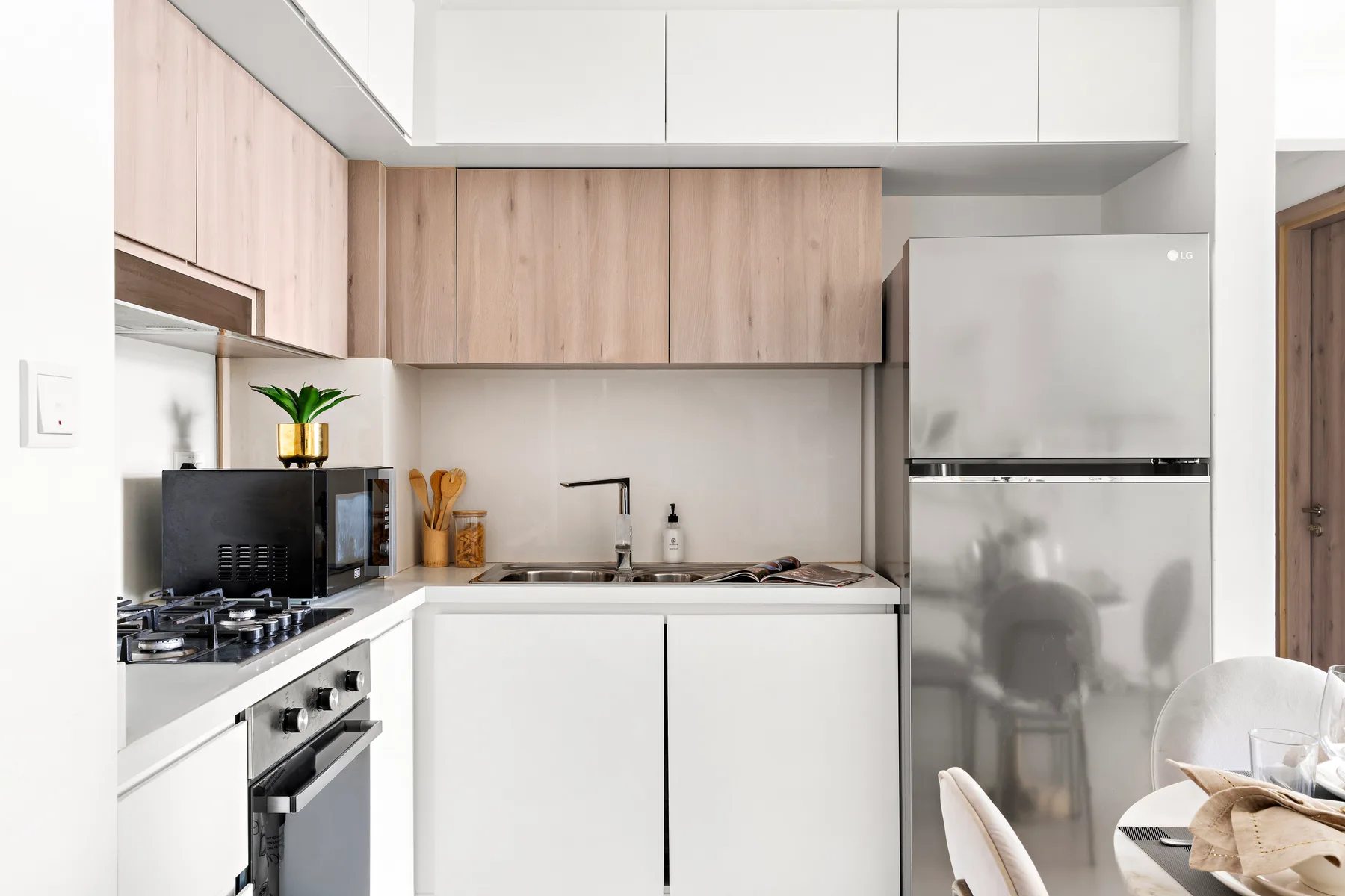 A modern kitchen with white cabinets, wood-finish cupboards, and stainless steel appliances.