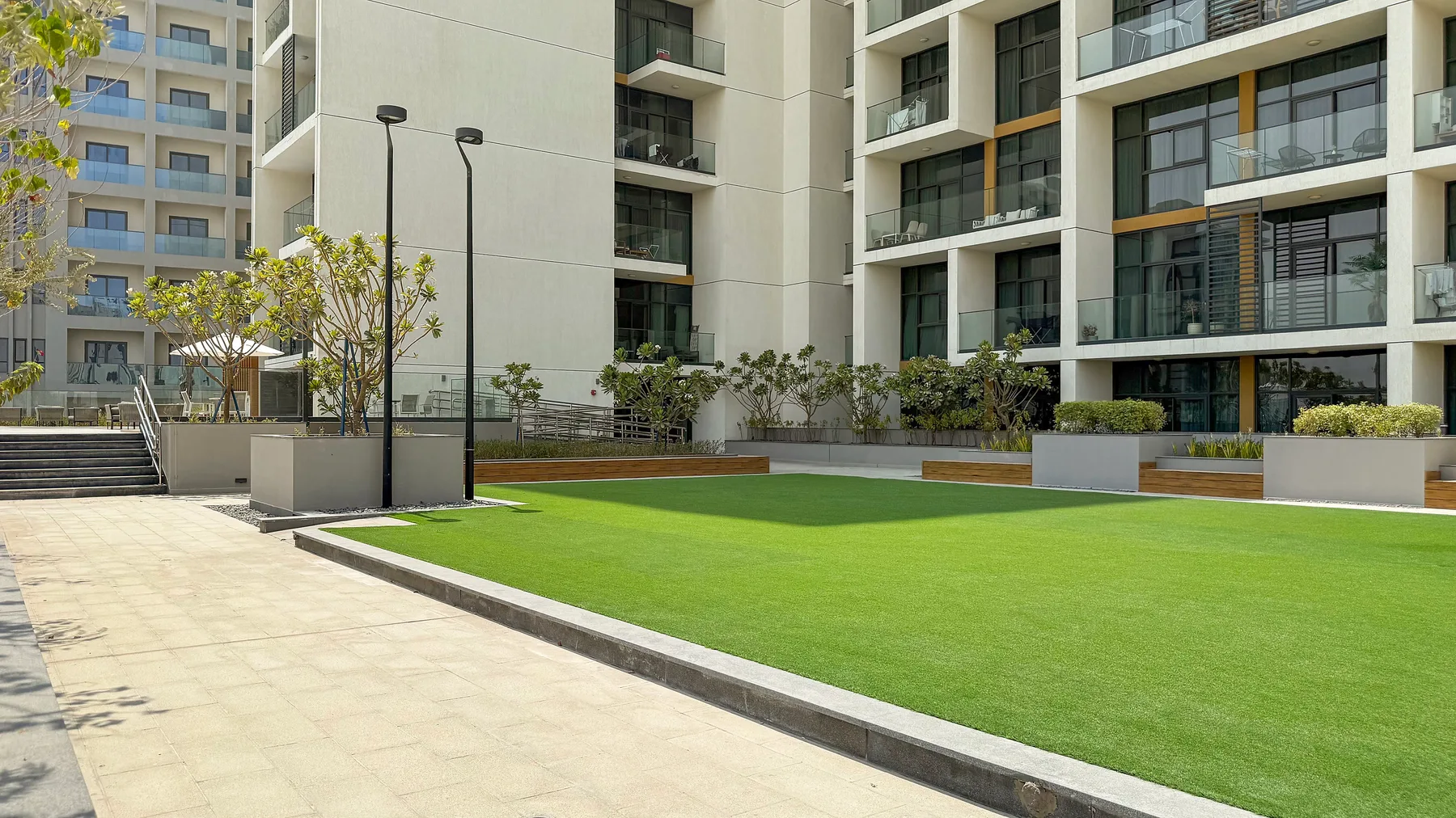 A landscaped courtyard beside a modern building, with a paved walkway and lawn.