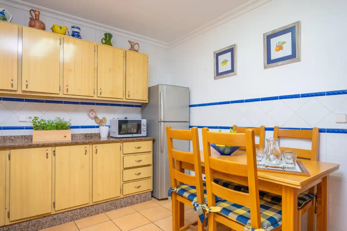 Una cocina con zona de comedor, armarios de madera, nevera y mesa.