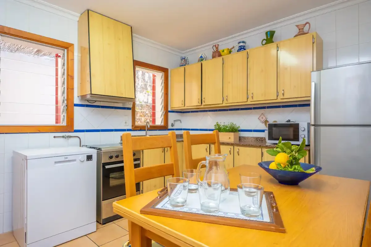 Una cocina luminosa con armarios de madera y una mesa preparada con vasos.