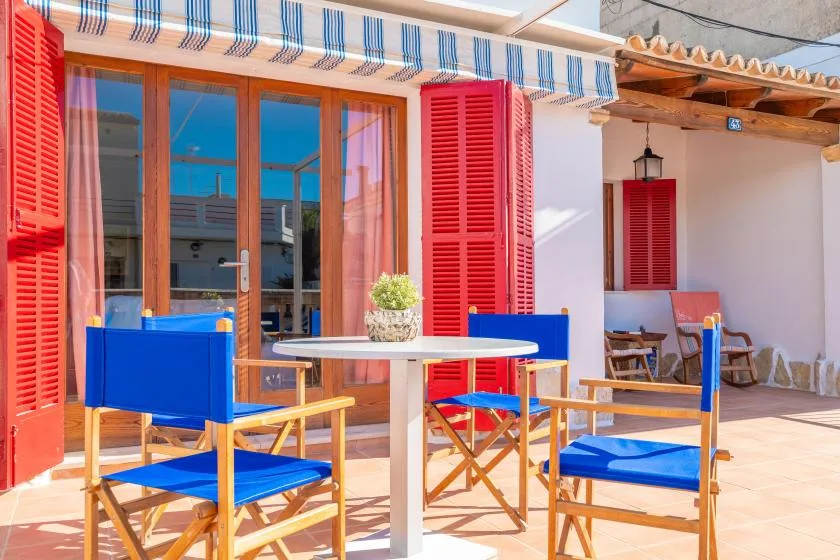 An outdoor patio with blue seating and a table beside red shutters.