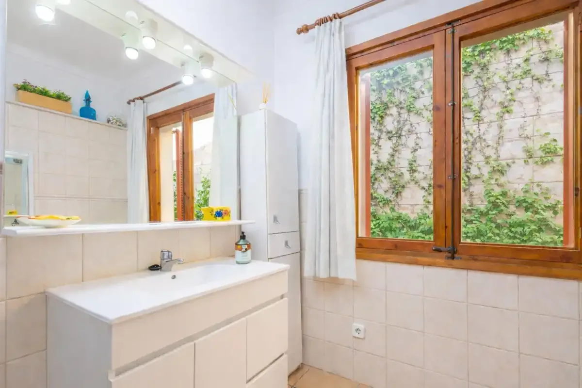 Un baño con azulejos, un lavabo con mueble y una ventana de marco de madera.