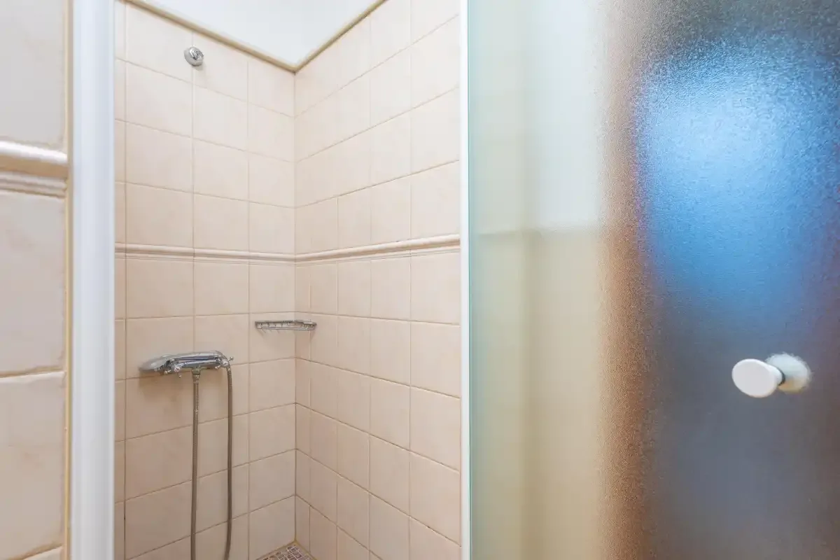 Una zona de ducha con azulejos junto a una puerta de vidrio esmerilado.