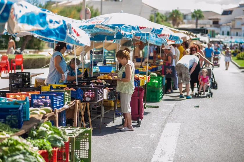Un puesto de mercado al aire libre exhibe productos en cajas bajo sombrillas coloridas.