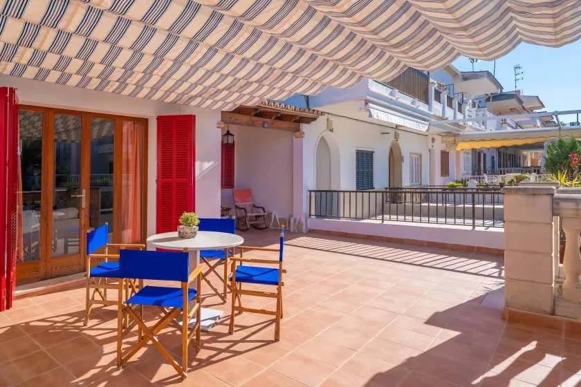 Una terraza soleada con toldo a rayas, una mesa y asientos azules.