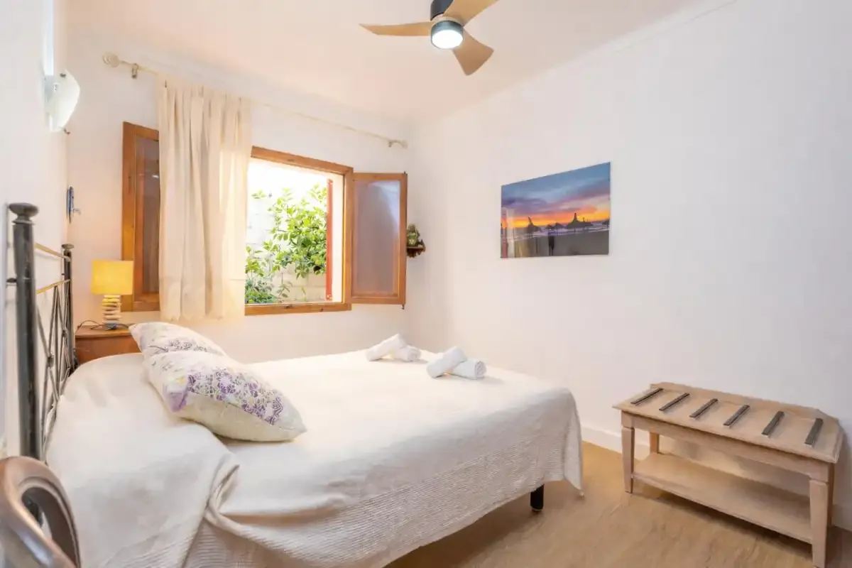 Un dormitorio con una cama bien arreglada y una ventana abierta.