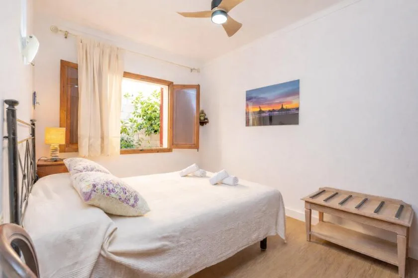 Un dormitorio con una cama bien tendida, una ventana abierta y un ventilador de techo.