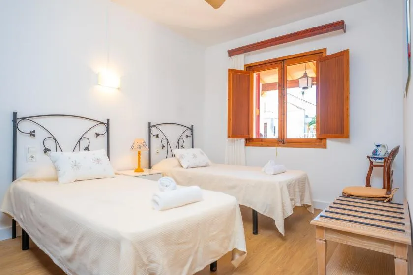 Un dormitorio luminoso con dos camas y una ventana de madera abierta.