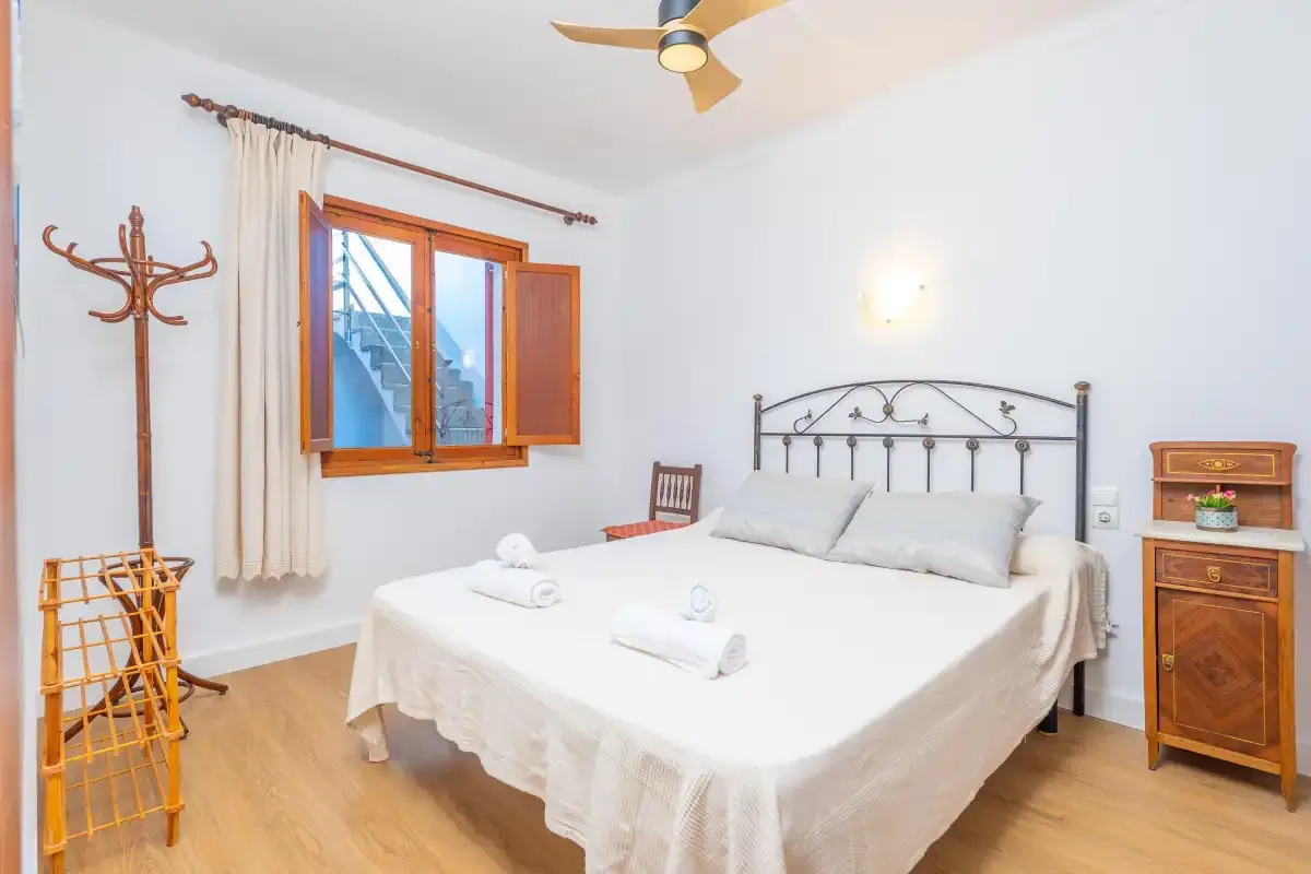 Un dormitorio con una cama doble, una ventana de madera abierta y un ventilador de techo.