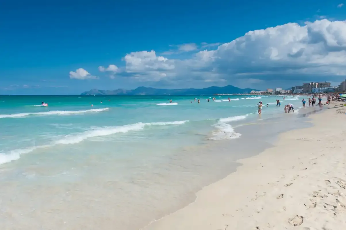 Una playa de arena se encuentra con aguas turquesas bajo un cielo parcialmente nublado.
