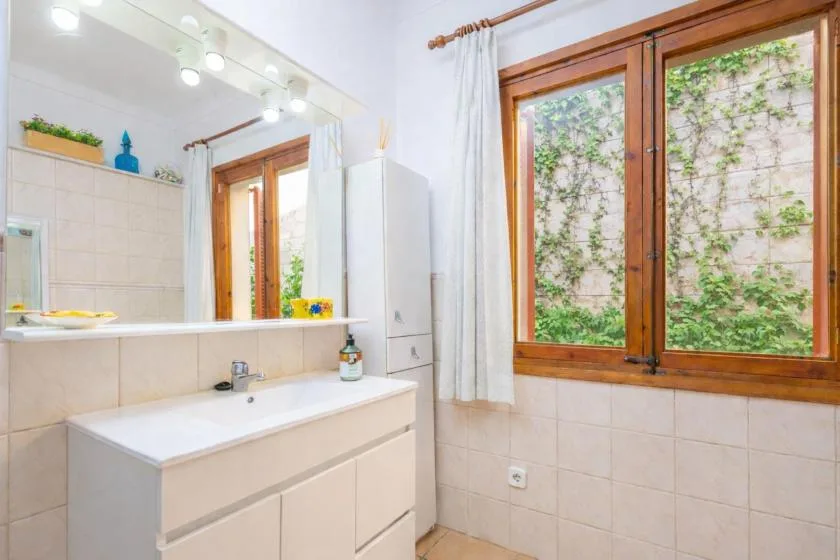 Un baño alicatado con lavabo, espejo y una gran ventana con marco de madera.