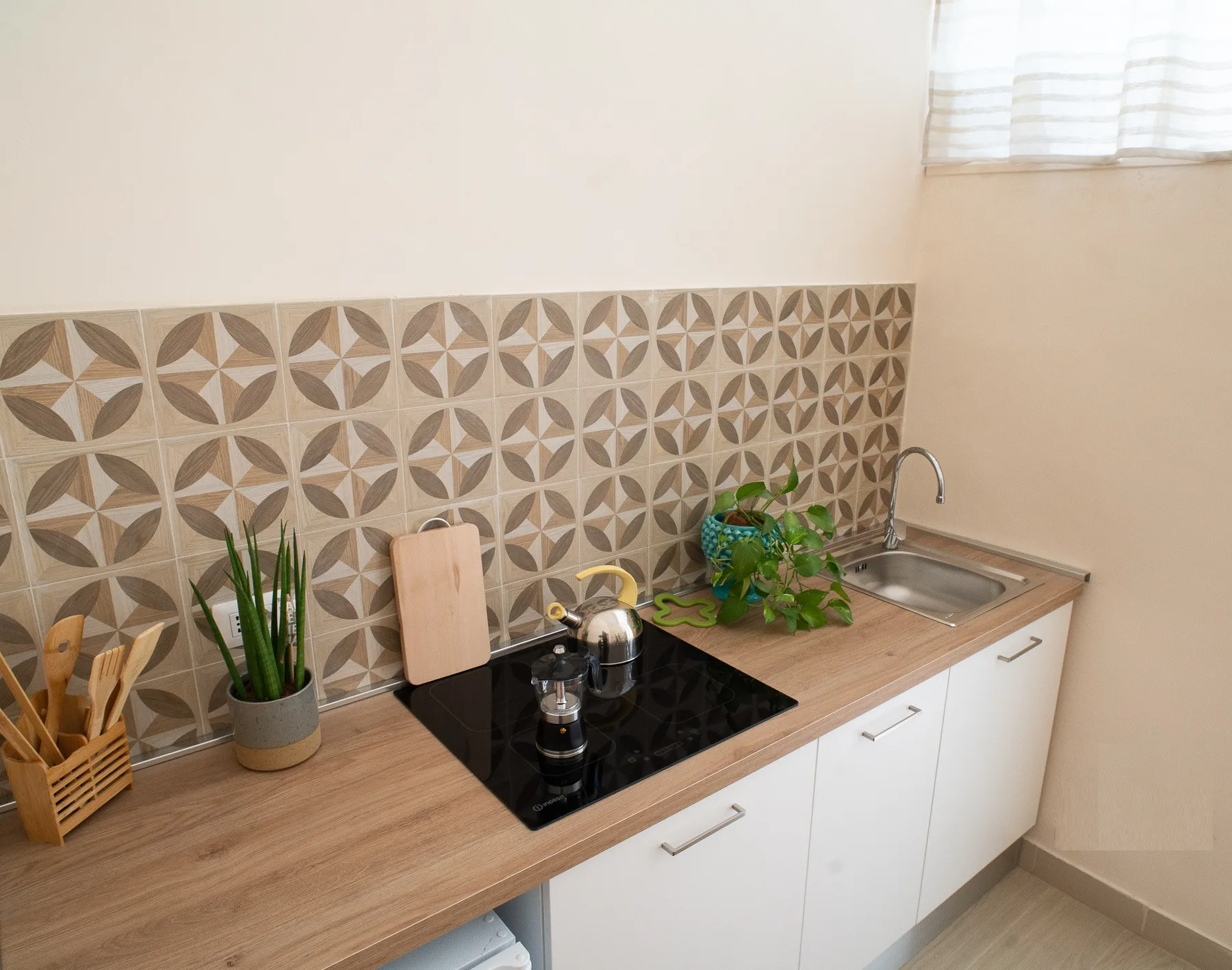 A kitchen counter with a cooktop, sink, and patterned tile backsplash.