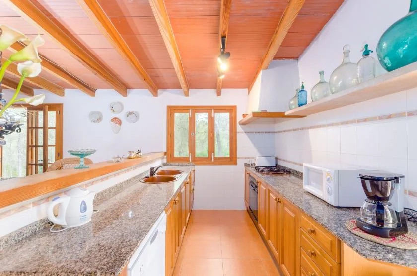 A narrow kitchen with wooden cabinets, stone counters, and exposed ceiling beams.
