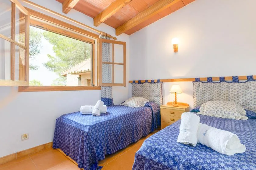 A bedroom with two beds dressed in blue patterned bedding and an open window.