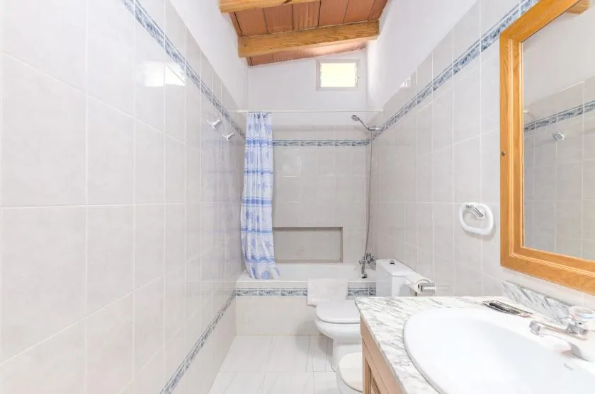 A tiled bathroom with a bathtub, toilet, and sink beneath a wooden ceiling.