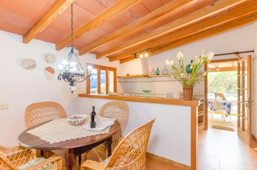 A dining area with wicker seating sits beside a kitchen counter and open glass doors.