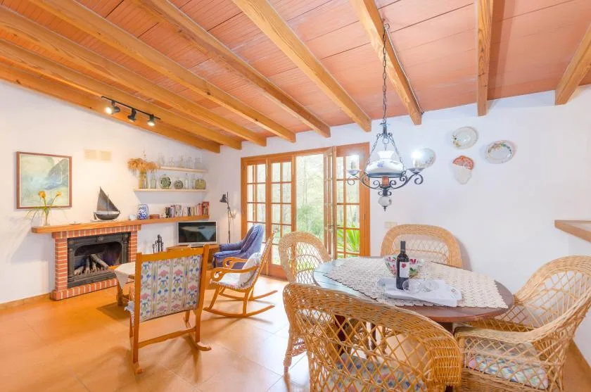 A dining and sitting room with wicker seating, a fireplace, and exposed wooden beams.
