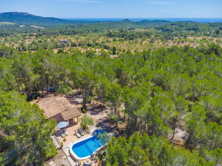 An aerial view of a swimming pool beside a house among wooded hills.