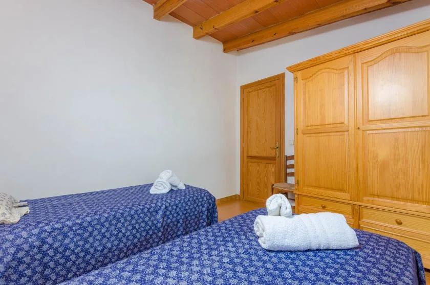 A bedroom with two blue patterned beds and wooden wardrobes.