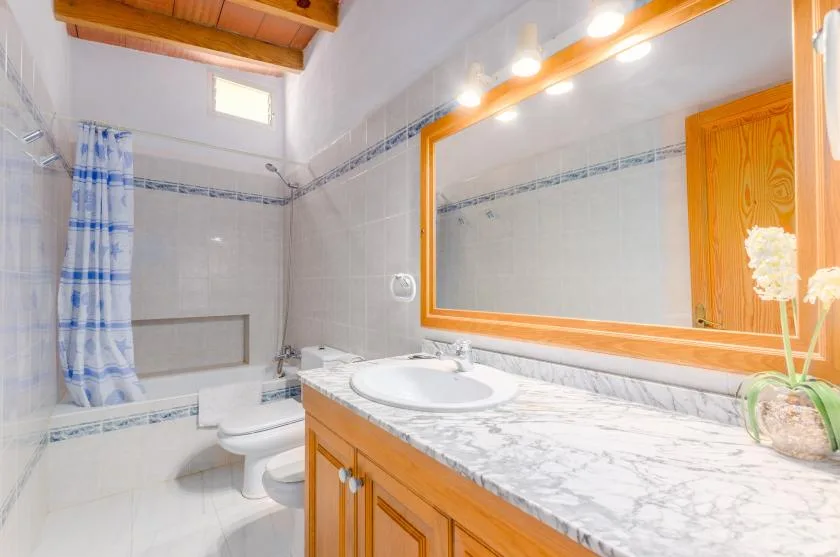 A tiled bathroom with a wooden vanity, large mirror, and shower curtain.