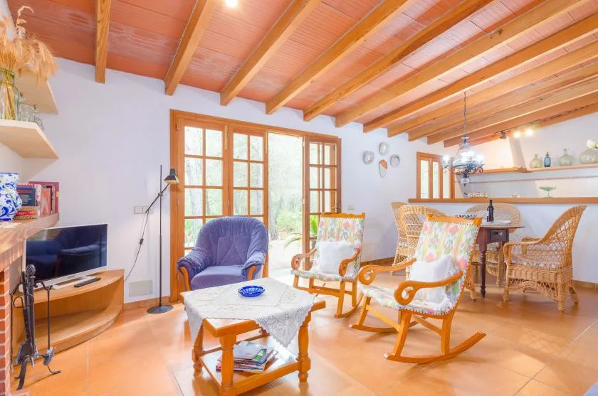 A bright living room with wooden seating, a television, and a dining area.